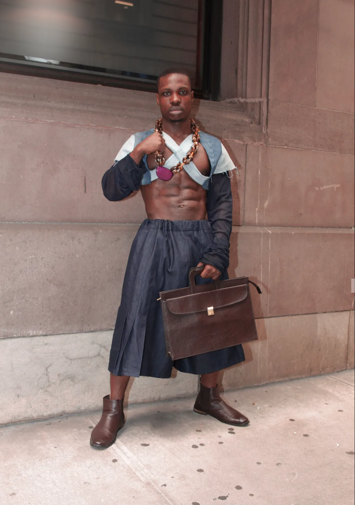 Model in a denim skirt and cropped jacket, carrying a leather briefcase.
